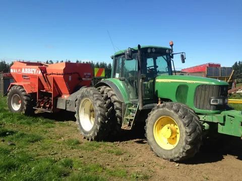 John Deere tractor hitched to an orange Abbey muck spreader in a yard