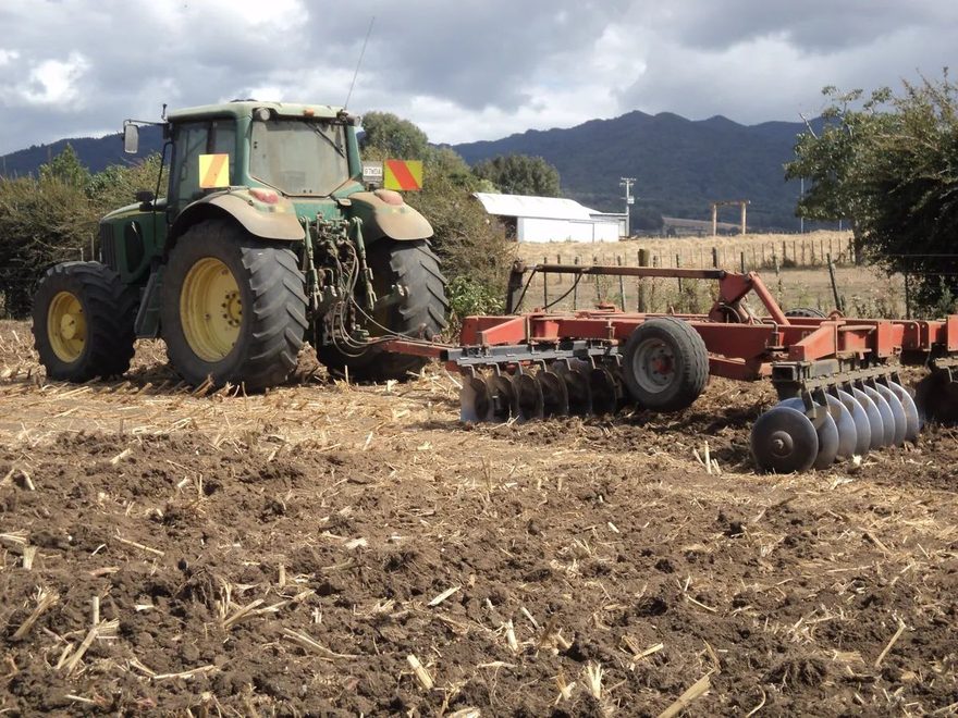 John Deere tractor with red discs on a paddock of worked-up maize stubble