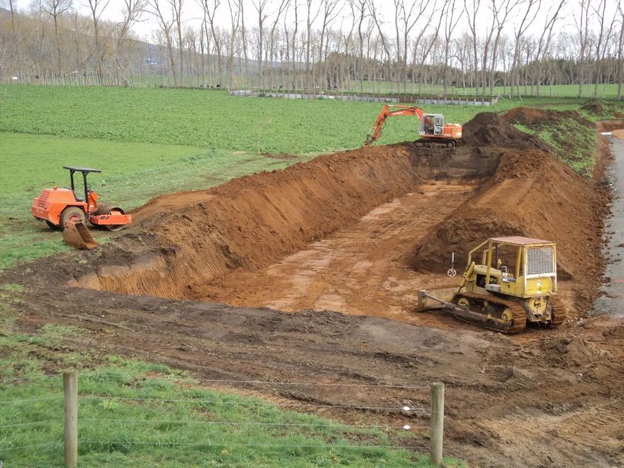 Bulldozer working in the bottom of a large rectangular pit dug into a green paddock